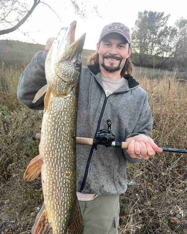 An Obalus owner on the bank holding a big pike and his casting rod