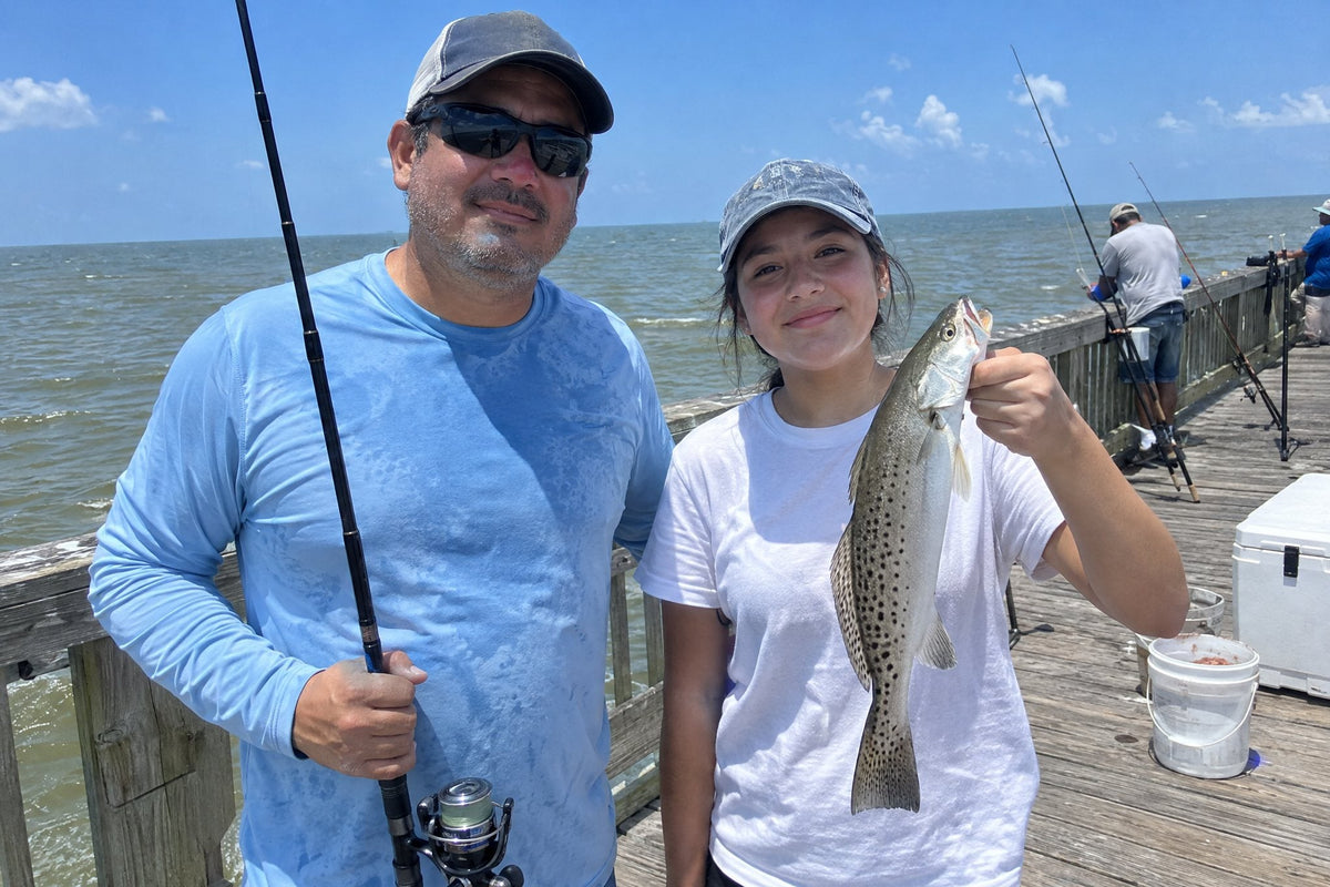 Father and teenage daughter on a sunny Gulf Coast fishing pier holding a speckled trout