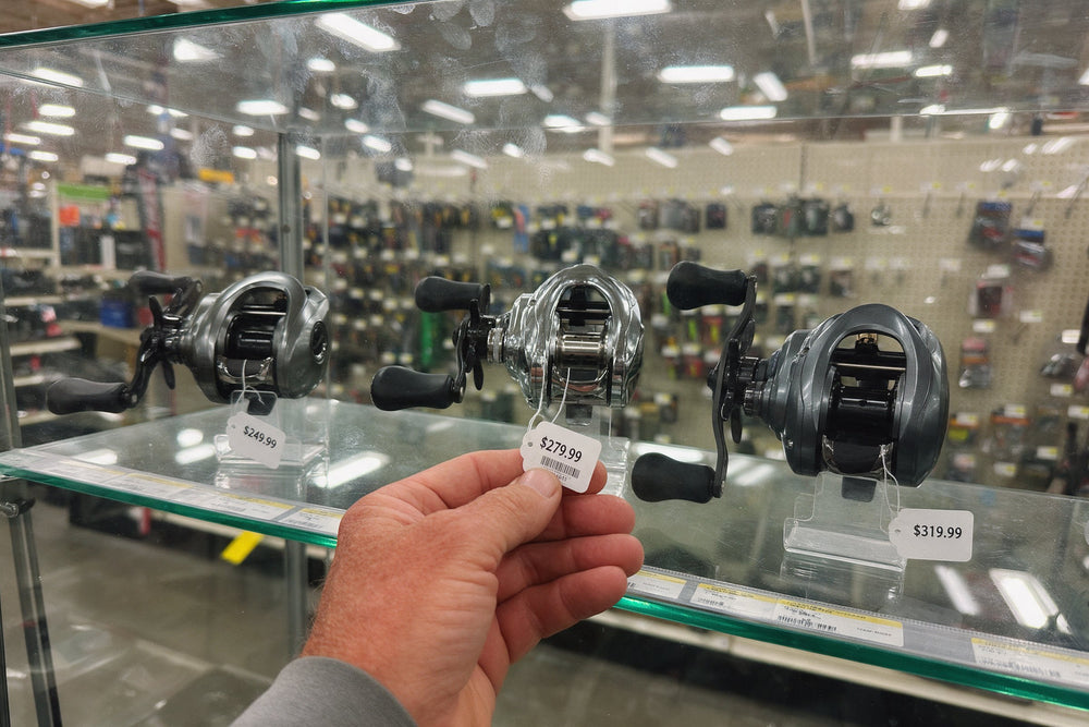 Baitcast reels in a store display case with $249.99, $279.99 and $319.99 price tags, one held in a hand