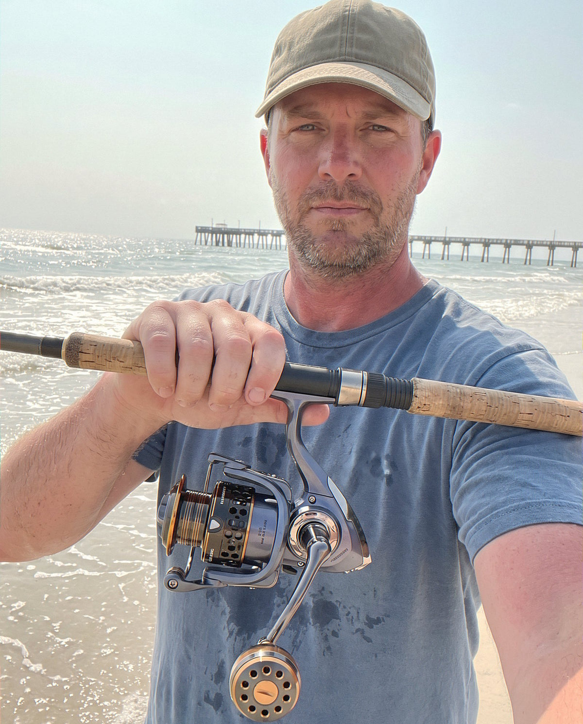 An angler on a Gulf beach holding a surf rod with the Obalus Gold Hex Pro reel
