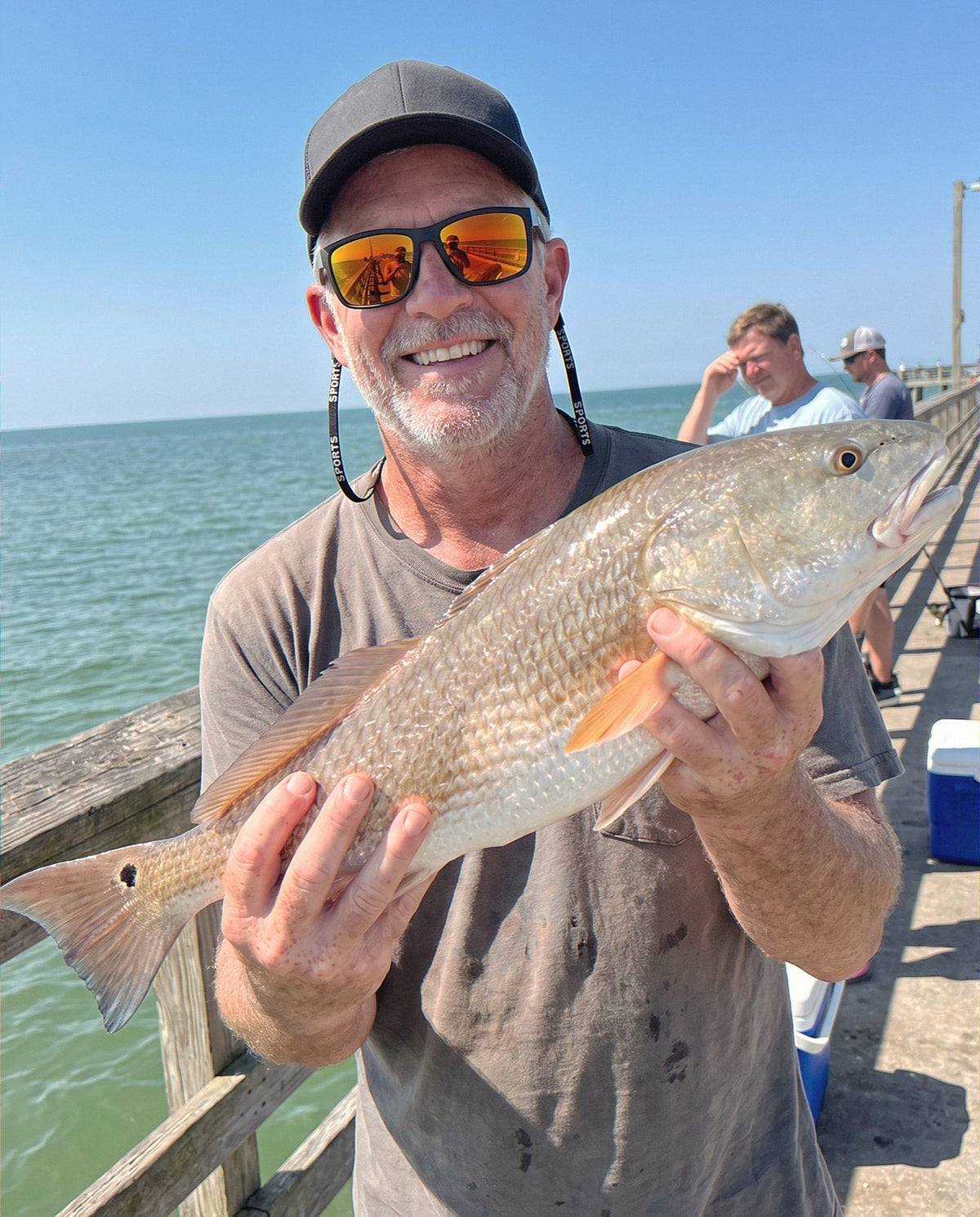An angler wearing the Obalus polarized sunglasses holds up a redfish on a pier