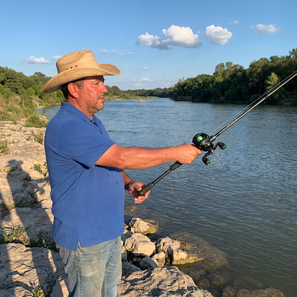 Man in a straw hat casting a baitcaster from a rocky riverbank