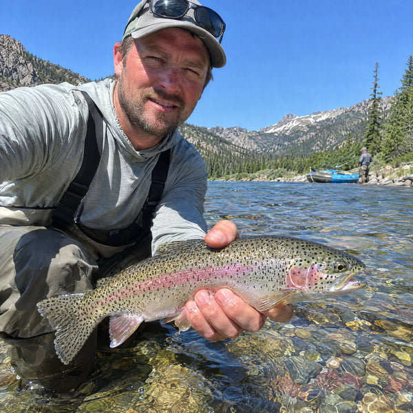 Angler kneeling in a clear mountain river holding a rainbow trout