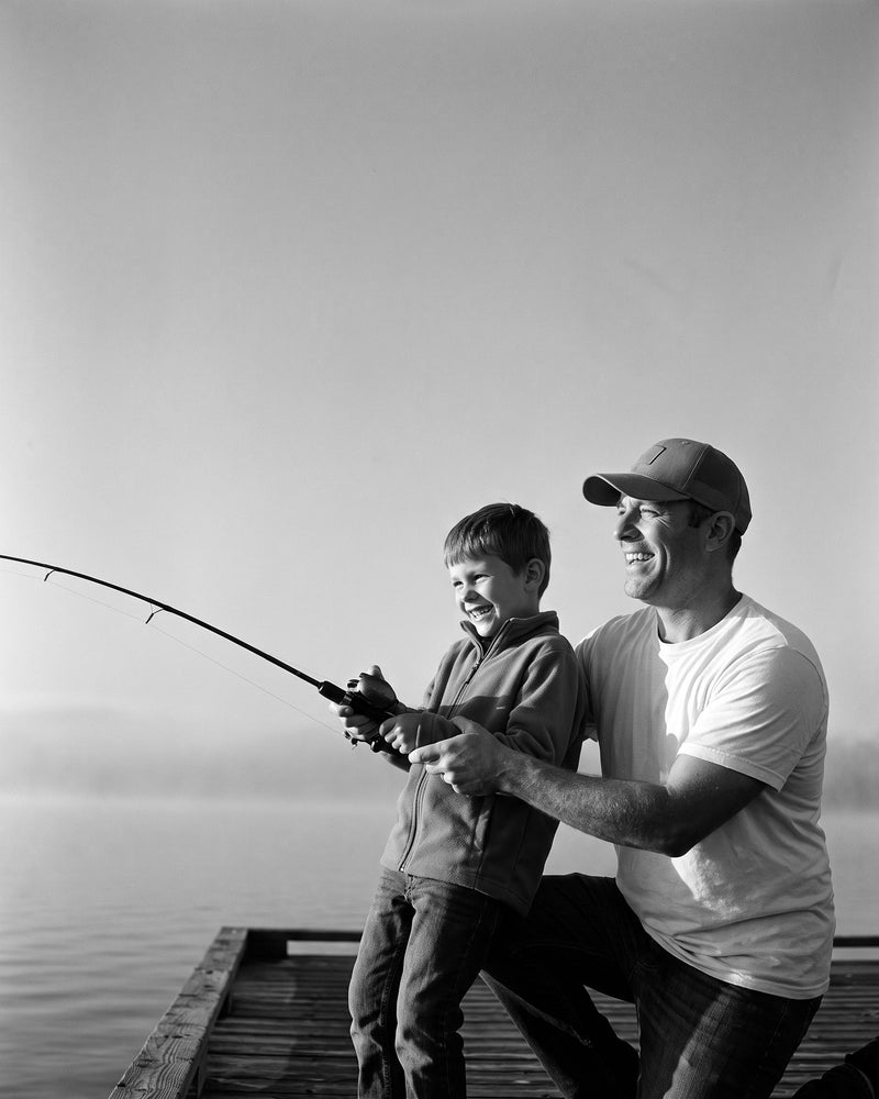 Black-and-white photo of an angler in a kayak among cypress trees holding up a big largemouth bass