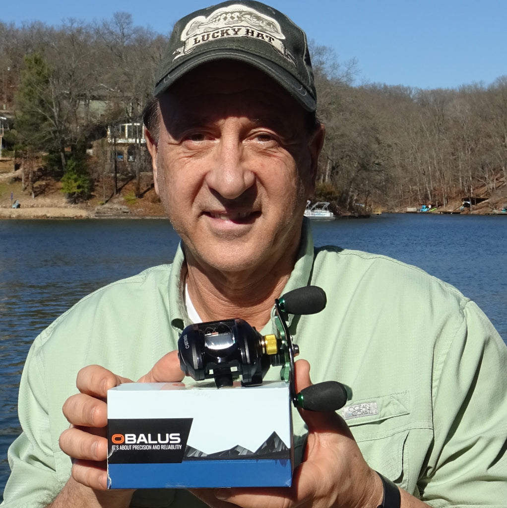 Person holding a fishing reel box by a lake.